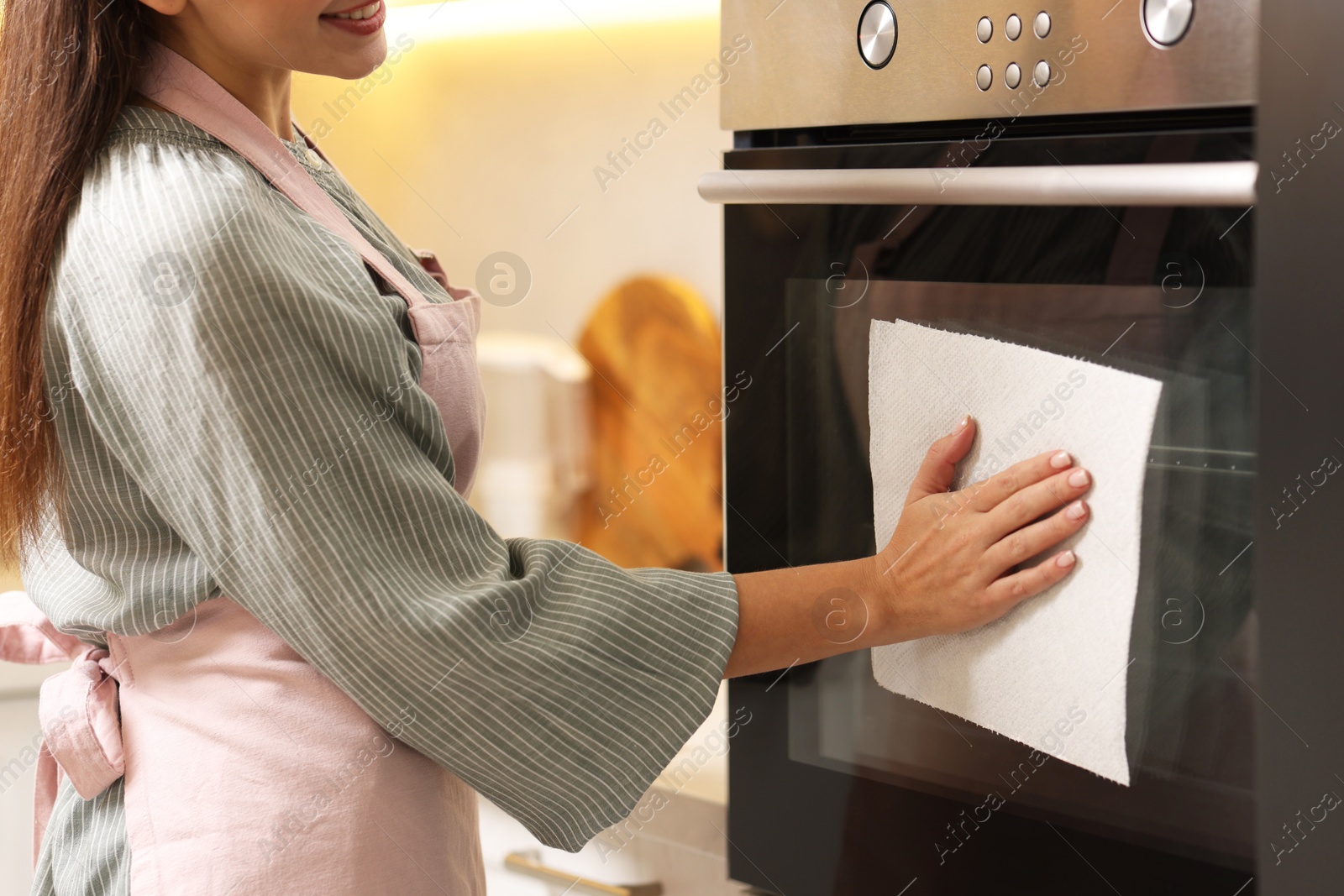 Photo of Woman wiping oven with paper towel in kitchen, closeup