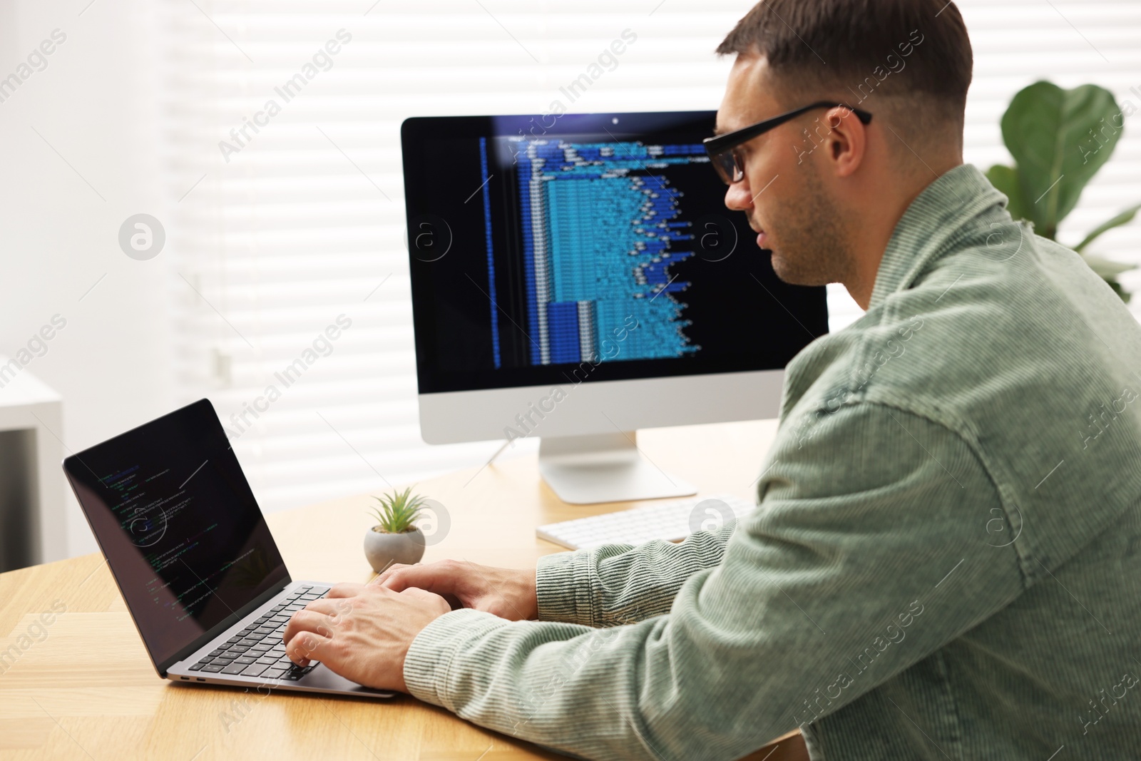 Photo of Programmer working on laptop at wooden desk indoors