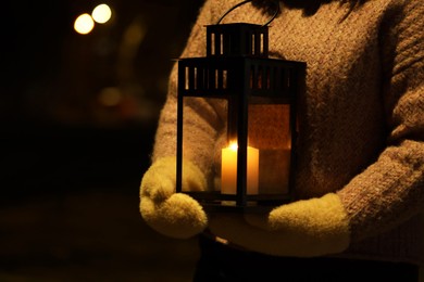 Photo of Woman holding Christmas lantern with burning candle in darkness, closeup. Space for text