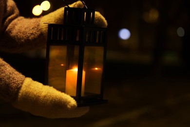 Photo of Woman holding Christmas lantern with burning candle in darkness, closeup. Space for text