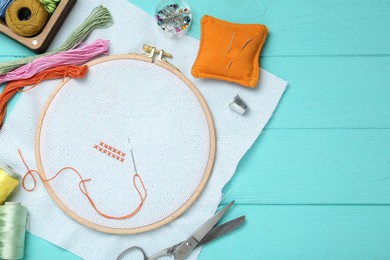 Photo of Embroidery. Canvas with cross stitches and supplies on turquoise wooden table, flat lay