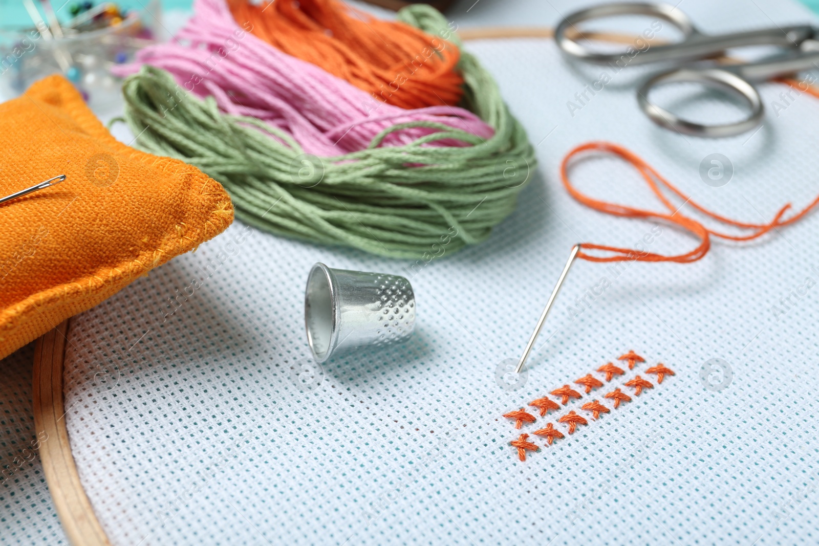 Photo of Embroidery. Canvas with cross stitches and supplies on table, closeup