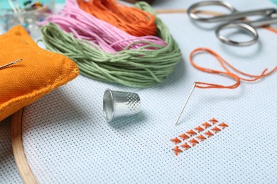 Photo of Embroidery. Canvas with cross stitches and supplies on table, closeup