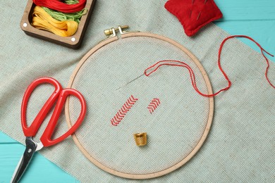 Photo of Embroidery. Canvas with cross stitches and supplies on turquoise wooden table, flat lay