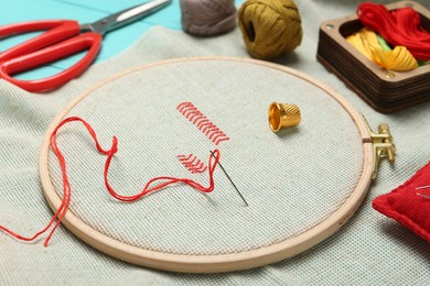 Photo of Embroidery. Canvas with cross stitches and supplies on turquoise table, closeup