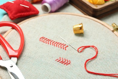 Photo of Embroidery. Canvas with cross stitches and supplies on table, closeup