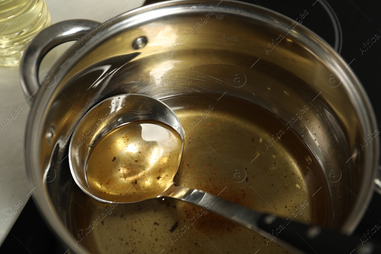 Photo of Used cooking oil and ladle in saucepan on stove, closeup