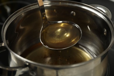 Photo of Pouring used cooking oil from ladle into saucepan, closeup