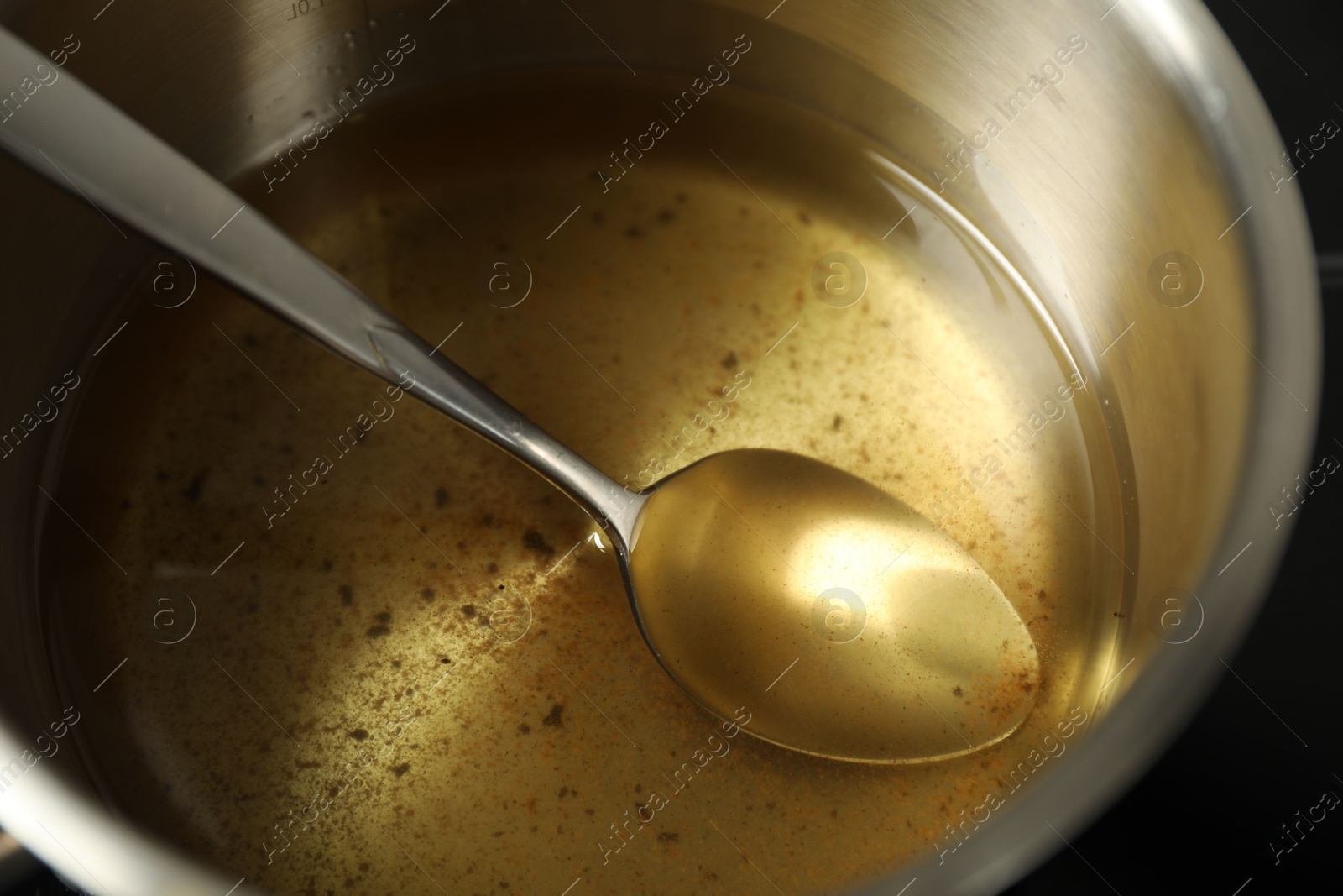 Photo of Used cooking oil and spoon in saute pan, closeup