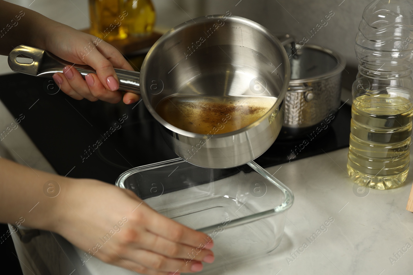 Photo of Woman pouring used cooking oil into glass container at white marble countertop, closeup