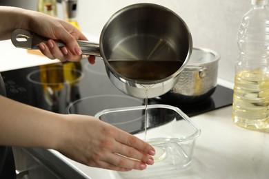 Photo of Woman pouring used cooking oil into glass container at white marble countertop, closeup