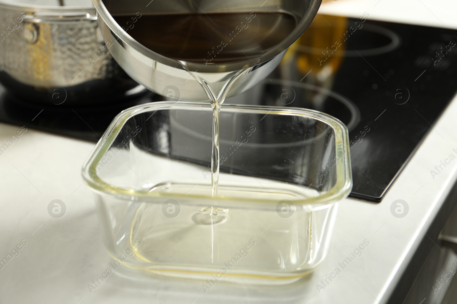 Photo of Pouring Used cooking oil into glass container at white countertop, closeup