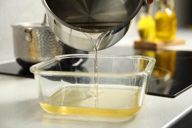 Photo of Pouring Used cooking oil into glass container at white countertop, closeup