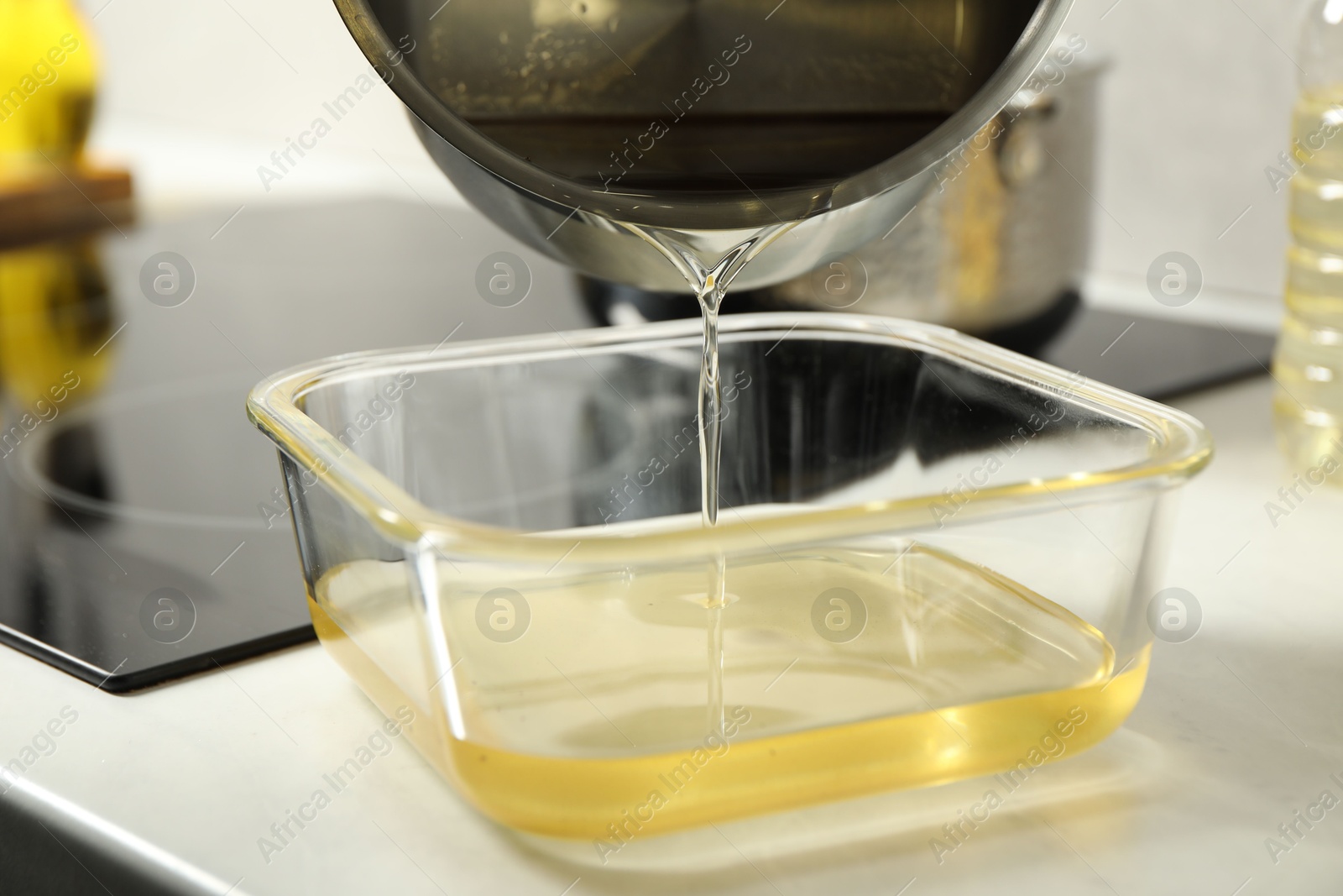 Photo of Pouring Used cooking oil into glass container at white countertop, closeup