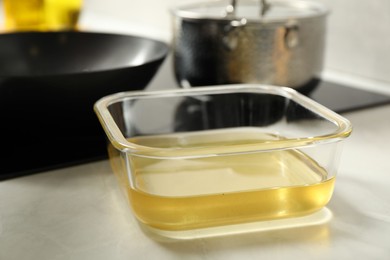 Photo of Used cooking oil in glass container on white marble countertop, closeup