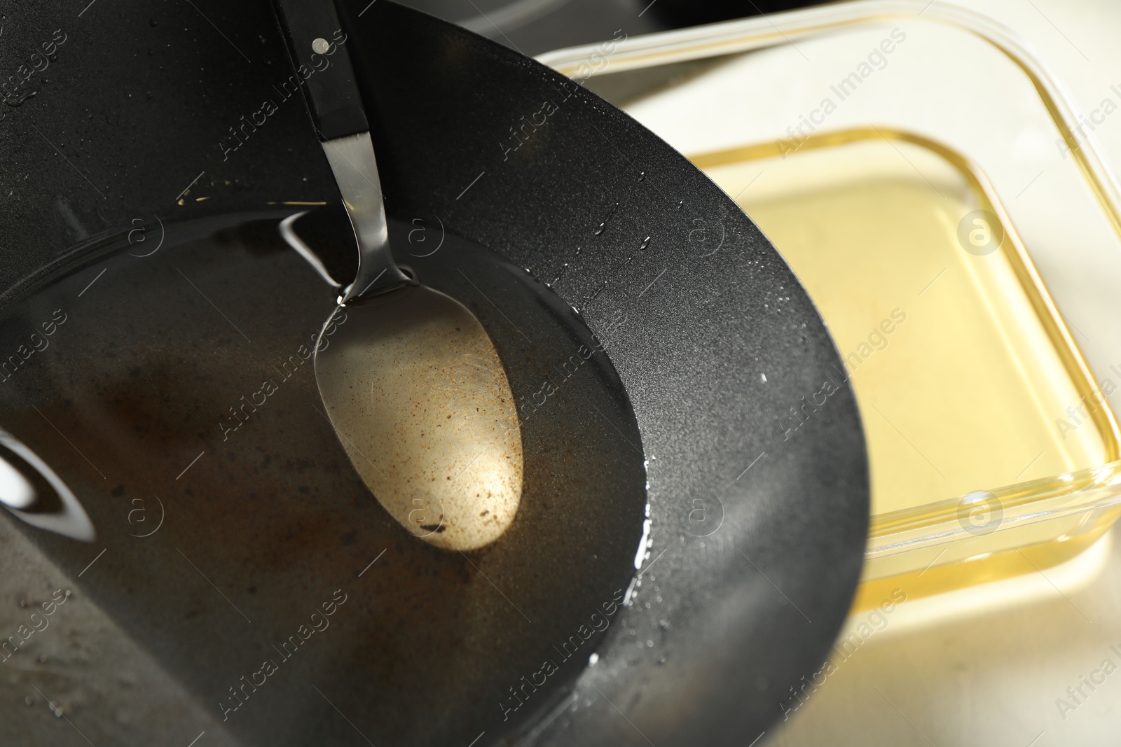 Photo of Used cooking oil and spoon in wok on white table, closeup