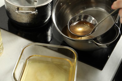 Photo of Woman pouring used cooking oil at white countertop, closeup