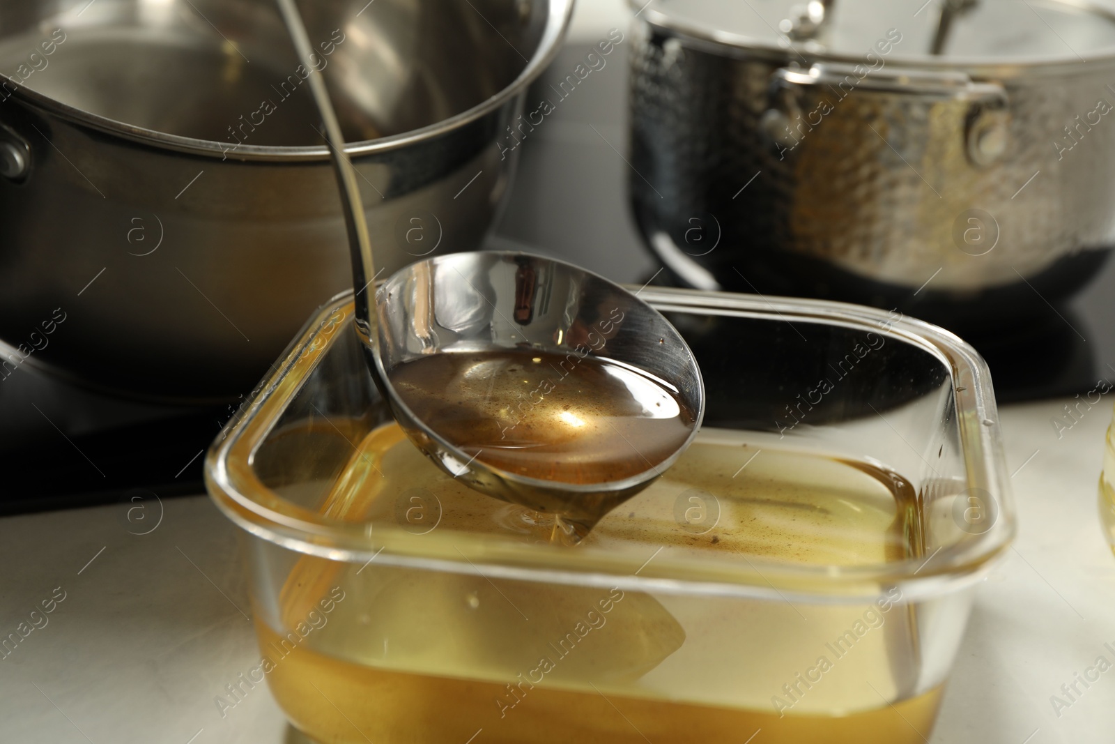 Photo of Pouring used cooking oil into glass container at white countertop, closeup