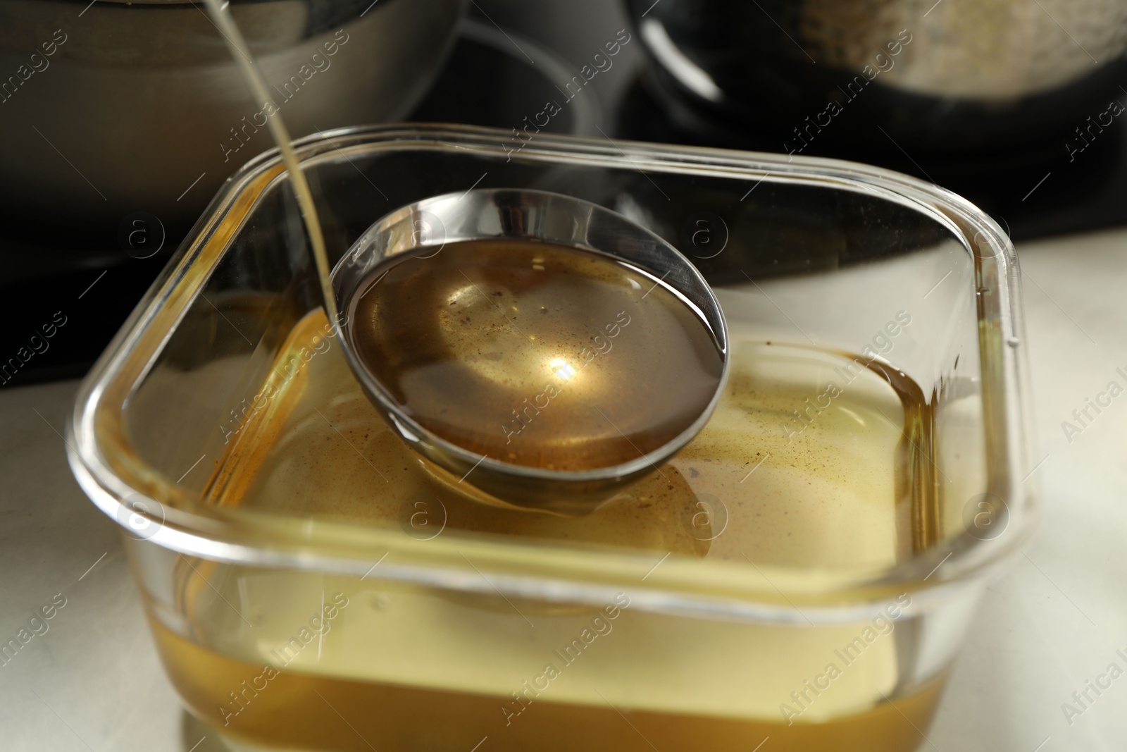 Photo of Used cooking oil in glass container and ladle on white countertop, closeup