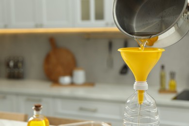 Photo of Pouring used cooking oil into bottle through funnel in kitchen, closeup. Space for text