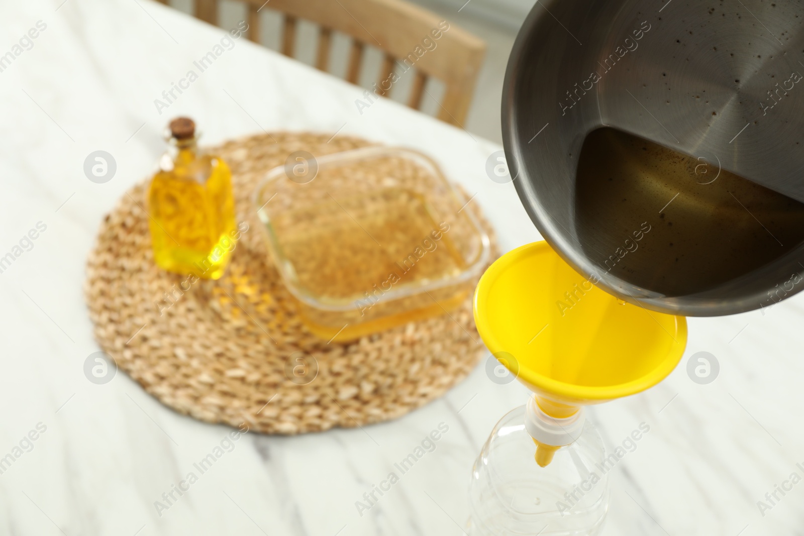 Photo of Pouring used cooking oil into bottle through funnel at white table in kitchen