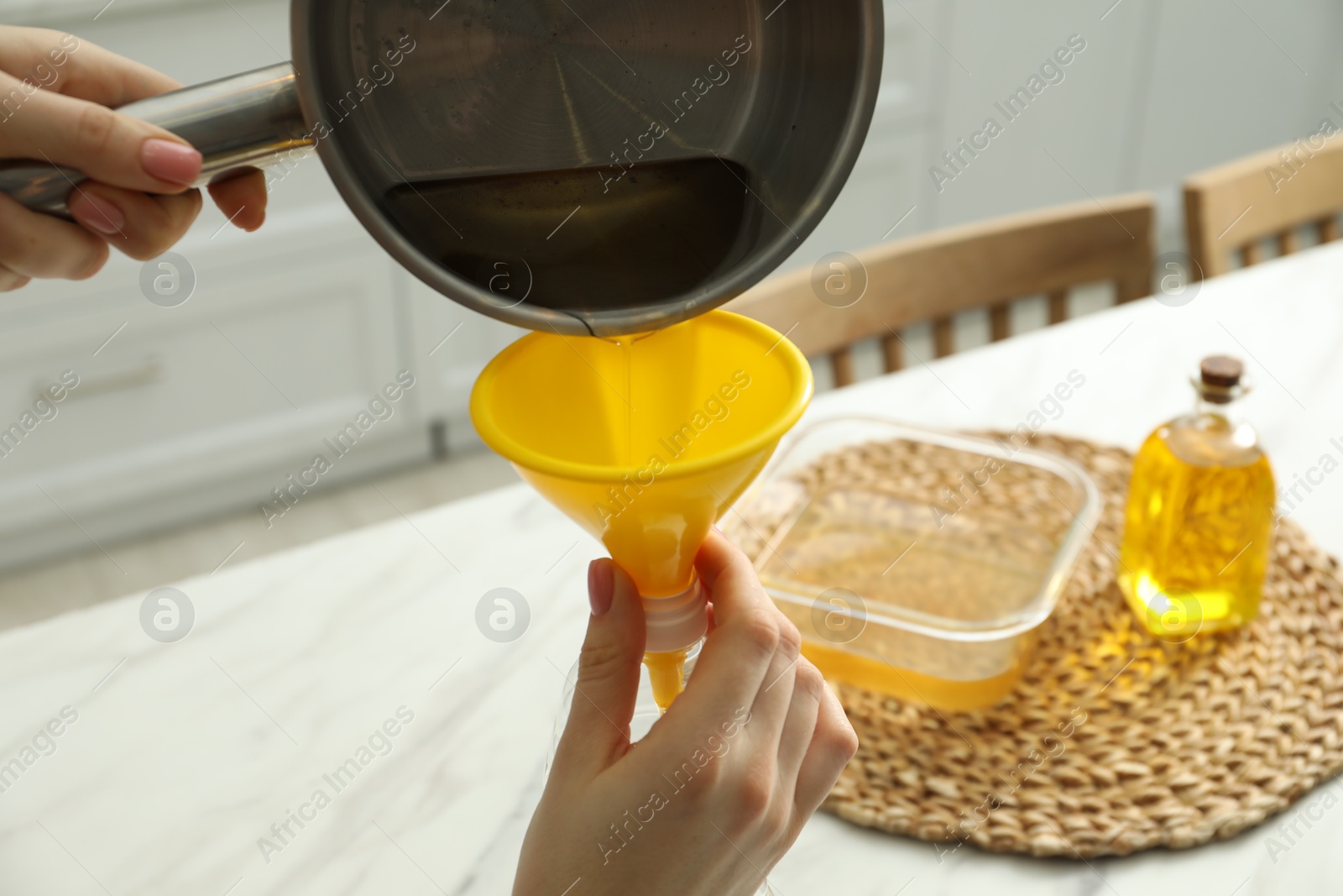 Photo of Woman pouring used cooking oil into bottle through funnel in kitchen, closeup