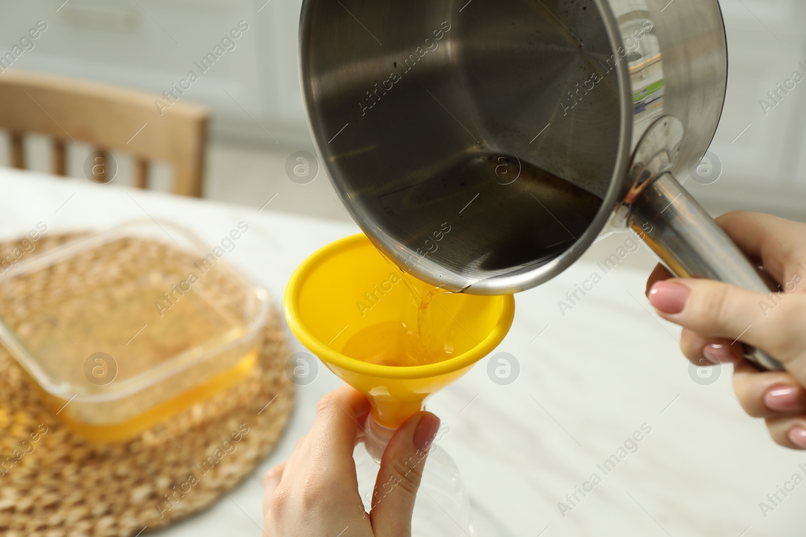 Photo of Woman pouring used cooking oil into bottle through funnel in kitchen, closeup