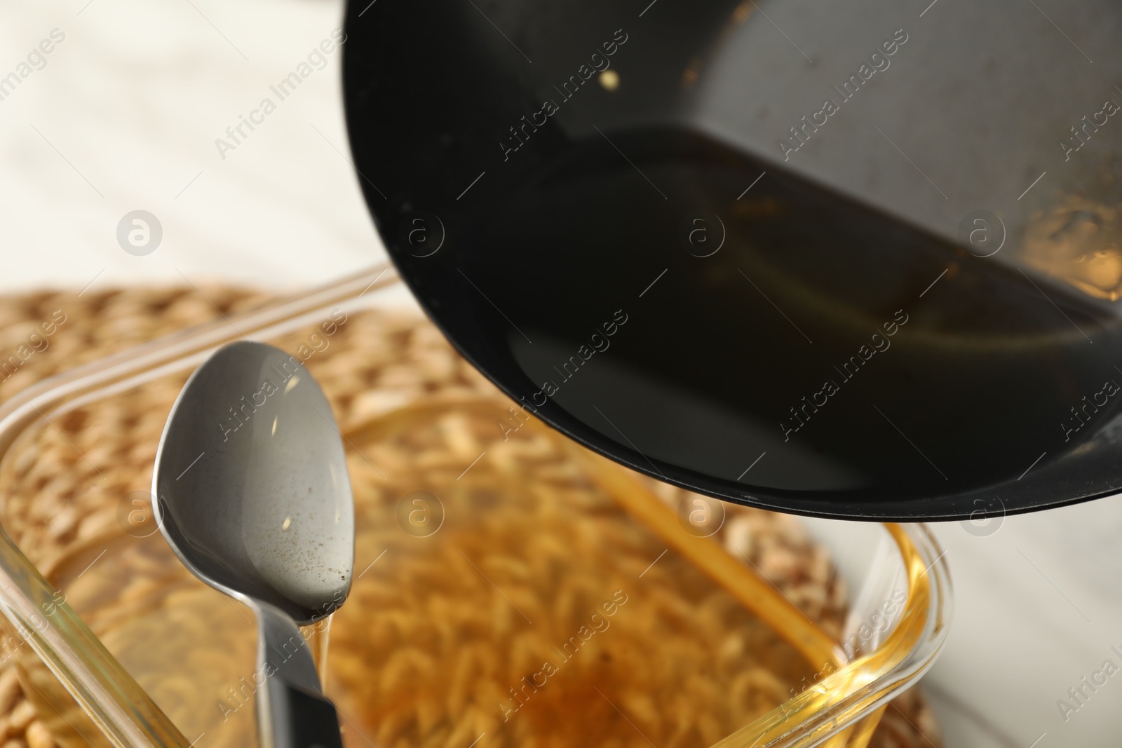 Photo of Pouring used cooking oil into glass container at white table, closeup