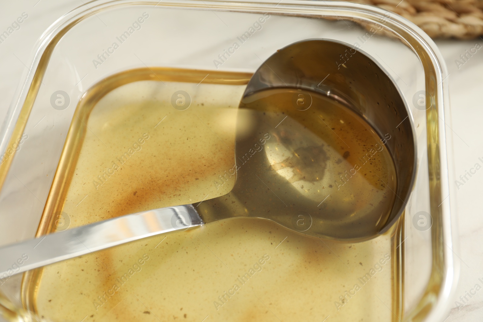 Photo of Used cooking oil and ladle in glass container on white table, closeup