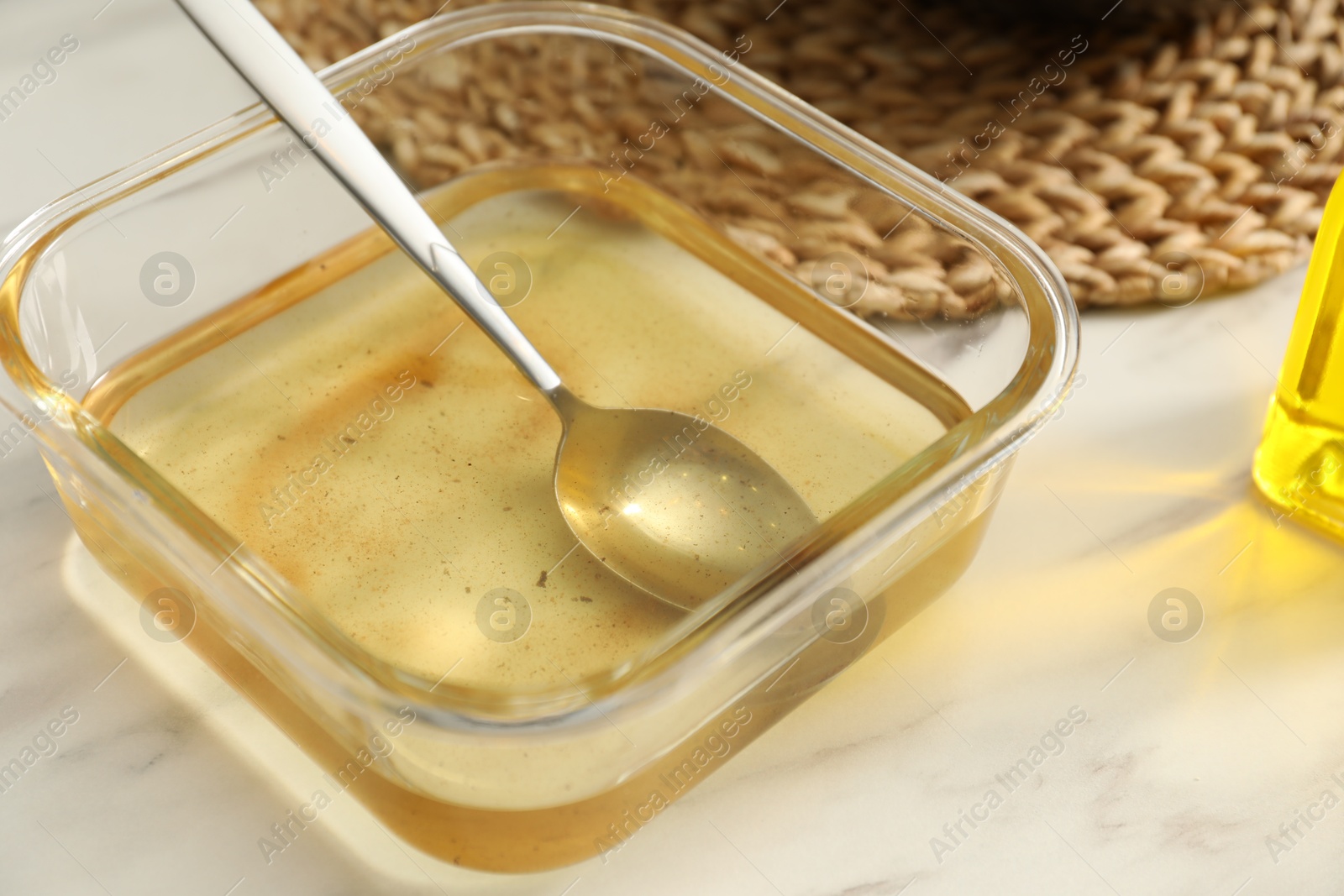 Photo of Used cooking oil and spoon in glass container on white marble table, closeup