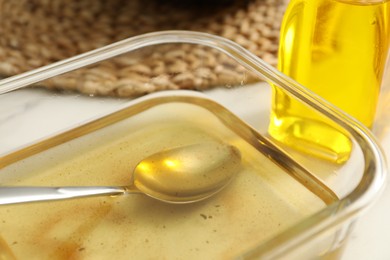 Photo of Used cooking oil and spoon in glass container on white table, closeup