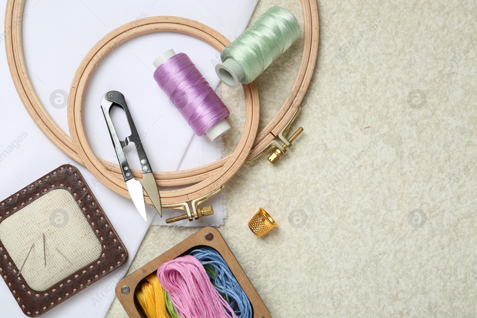 Photo of Embroidery. Different sewing accessories on beige textured table, flat lay. Space for text