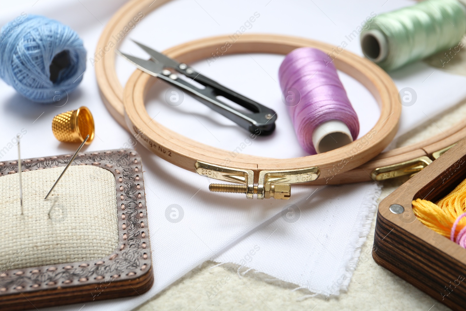 Photo of Embroidery. Different sewing accessories on beige textured table, closeup