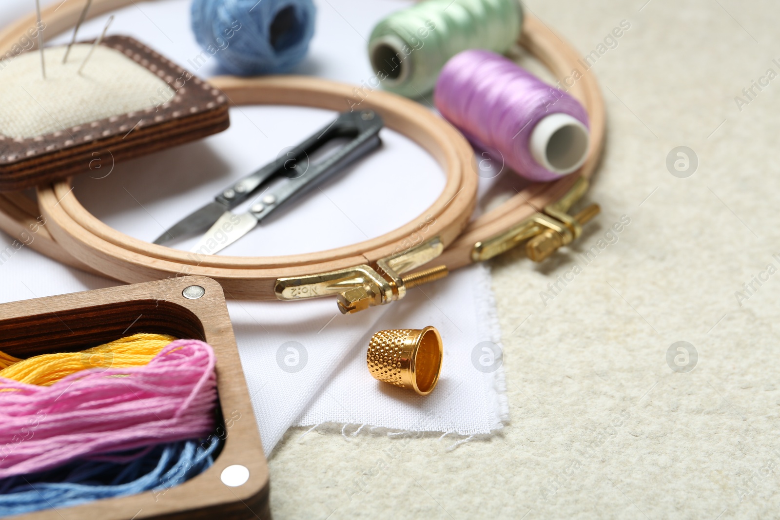 Photo of Embroidery. Different sewing accessories on beige textured table, closeup. Space for text