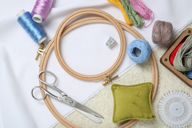 Photo of Embroidery. Different sewing accessories on beige textured table, flat lay