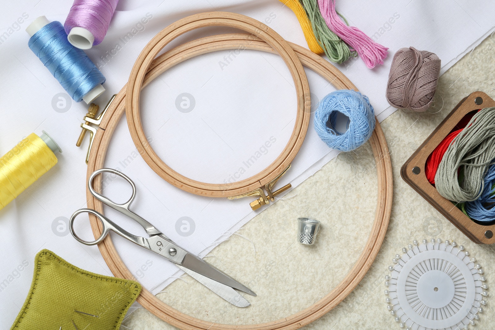 Photo of Embroidery. Different sewing accessories on beige textured table, flat lay