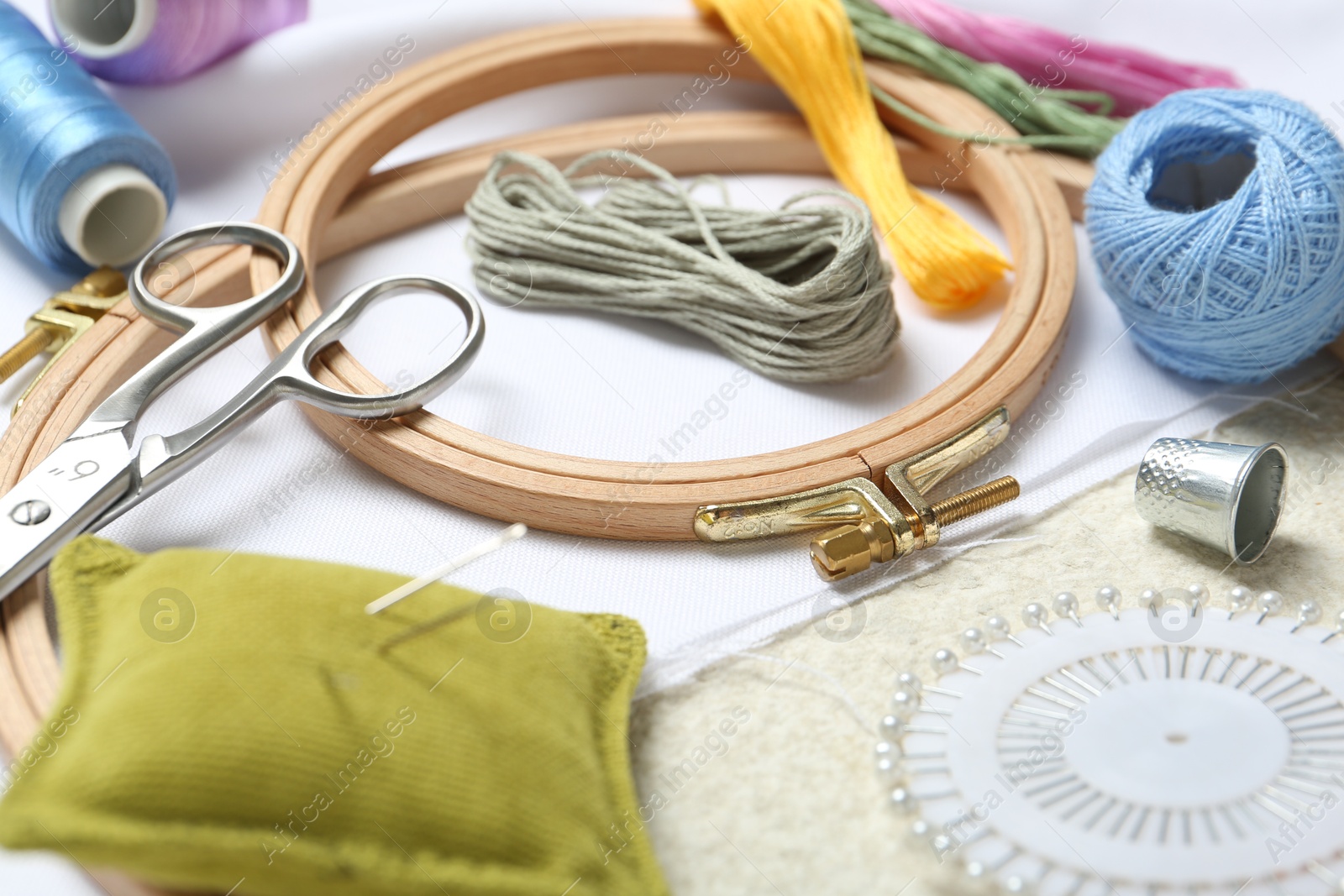 Photo of Embroidery. Different sewing accessories on beige textured table, closeup