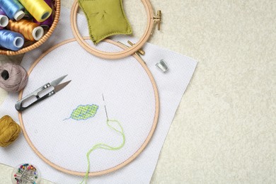 Photo of Embroidery and different sewing accessories on beige textured table, flat lay. Space for text