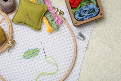 Photo of Embroidery and different sewing accessories on beige textured table, flat lay