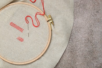 Photo of Canvas with embroidery in hoop on grey table, top view. Space for text