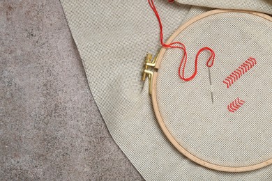 Canvas with embroidery in hoop on grey table, top view. Space for text