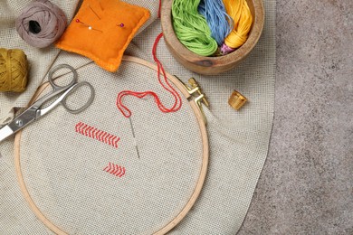 Photo of Embroidery and different sewing accessories on grey table, flat lay