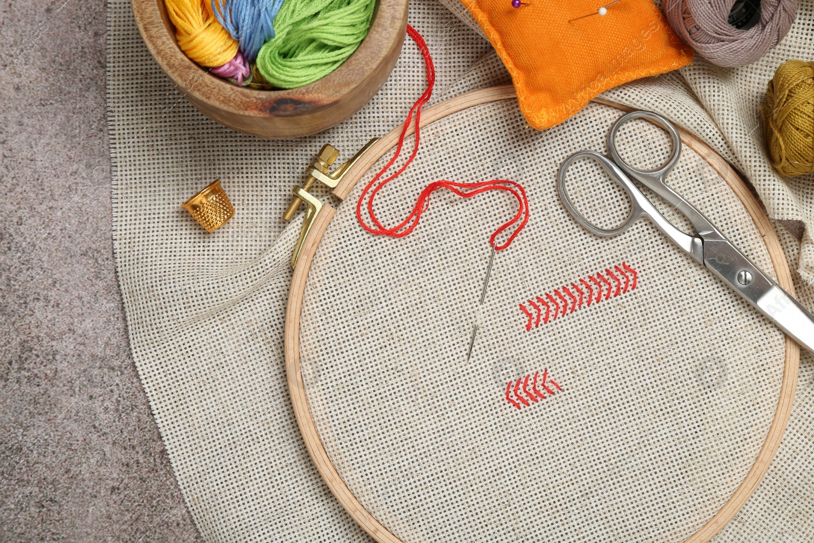 Photo of Embroidery and different sewing accessories on grey table, flat lay