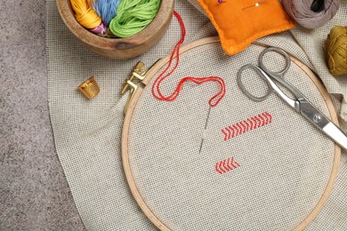 Photo of Embroidery and different sewing accessories on grey table, flat lay