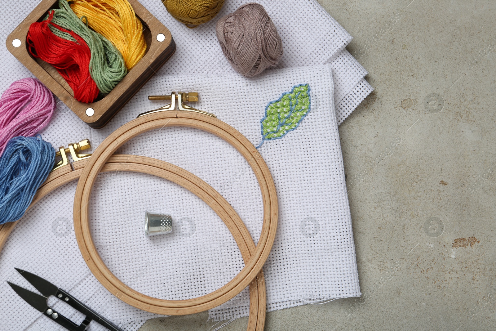 Photo of Embroidery and different sewing accessories on grey table, flat lay. Space for text