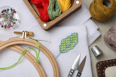 Photo of Embroidery and different sewing accessories on grey table, flat lay