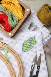 Photo of Embroidery and different sewing accessories on grey table, flat lay