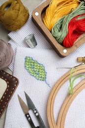 Photo of Embroidery and different sewing accessories on grey table, flat lay