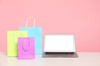 Photo of Internet shopping. Laptop and colorful paper bags on table against pink background