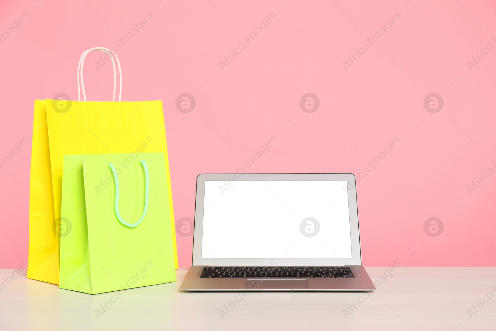 Photo of Internet shopping. Laptop and colorful paper bags on table against pink background